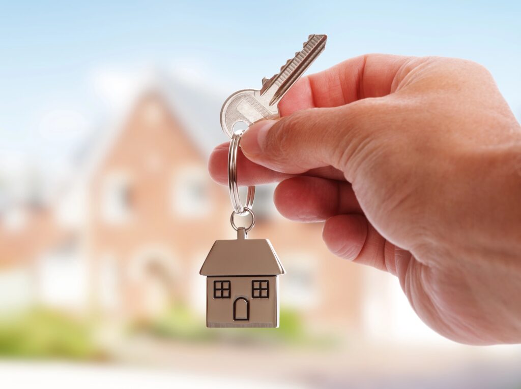 Hand holding house key in front of house