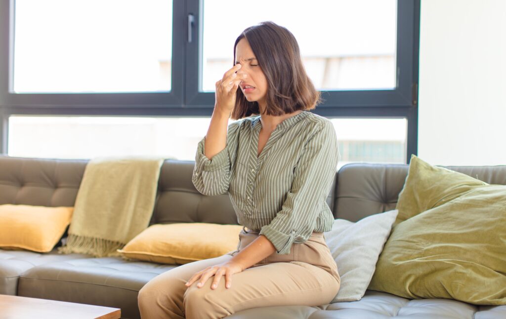 Young woman holding nose while sitting on couch at home